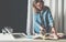 Office design studio, young businesswoman in denim shirt standing near desktop and leafing through catalog.