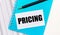 On the office desk there are reports, a blue notepad, a black pen, and a white card with the text PRICING. Stylish workplace.