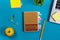 Office table desk with set of colorful supplies, white blank note pad, cup, pen, pc, crumpled paper, flower on blue