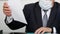 An official or businessman in a suit, tie and medical mask sits at a table and holds an important document in his hands