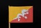 A official Flag of Bhutan on toothpick on black background. Consists of yellow and red side with white dragon
