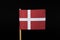 A official flag of Denmark on toothpick on black background. A red field charged with a white Nordic cross that extends to the