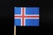 A official flag of Iceland on toothpick on black background. A blue field with the white-edged red Nordic cross that extends to