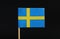 A official flag of Sweden on toothpick on black background. A blue field charged with a yellow Nordic cross that extends to the