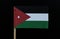 A official and unique flag of Jordan on toothpick on black background. A horizontal triband of black, white and green; with a red