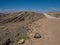 An offroad car driving on road trip on beautiful sunshine day through dusty unpaved route among desert rock mountain landscape