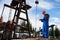 Oil engineer with a laptop standing next to an oil rig making notes in his computer