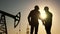 oil production. two silhouette workers work as a team next to an oil pump. business oil production production concept