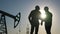 oil production. two silhouette workers work as a team next to an oil pump. business oil production production concept