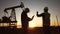 oil production. two workers a work next to an oil pump at sunset silhouette. industry business oil production concept