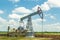 Oil pump in the field, beautiful blue sky with clouds. Russian oil production