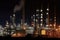 Oil refinery illuminated at night, with numerous pipelines and storage tanks depicting fossil fuel industry