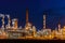 Oil refinery illuminated at night, with numerous pipelines and storage tanks depicting fossil fuel industry