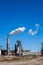 Oil refinery plant with chimney blowing smoke against a clear blue sky.
