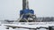 Oil rig with annexes among snow-covered landscape against cloudy sky in winter. Oil drilling rig operation on oil
