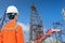 Oil rig worker wearing personal protective equipment looking at drilling rig while in operation for well completion activity