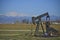 Oil well, pump jack with snow capped mountains