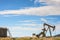 Oil Well And Tank Against Mountains and Blue Cloudy Sky