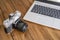 An old 35 mm reflex camera on a wooden table next to a modern laptop