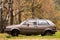 Old abandoned beige car without a wheel on the background of autumn nature