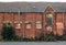 Old abandoned brick factory building with boarded up windows and crumbling decaying walls overgrown with weeds