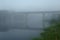 Old abandoned bridge over the river half-covered with predawn mist