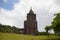 Old abandoned church in green field. Medieval ruin in summer landscape. Christian temple from brown stone.