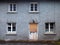 Old abandoned grey derelict house on a residential street with dirty broken windows and a boarded up door