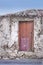 Old abandoned house or home with a weathered stone wall and red wooden door. Vintage and aged residential building built