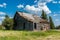 Old abandoned prairie farmhouse surrounded by trees, tall grass and blue sky