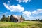 Old abandoned prairie farmhouse surrounded by trees, tall grass and blue sky