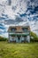 Old, abandoned prairie farmhouse with trees, grass and blue sky in Saskatchewan, Canada