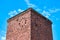 Old abandoned red brick tower with round clock on facade, vintage masonry, blue sky background