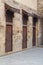 Old abandoned stone bricks wall with three weathered wooden doors covered with wooden grid