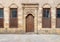 Old abandoned stone decorated bricks wall with arched wooden door and four shutter windows