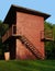 Old aged vintage small industrial windowless painted brick hut building with external metal staircase, a water pumping facility
