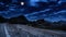 Old ancient castle on the hill at night. Rocky peaks of the ridge in the distant background in full moon light and cloudy sky