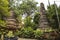 Old ancient pagoda of Thai temple surrounded with green plants trees and lot of small monk statues on the base of pagoda