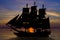 Old ancient pirate ship silhouette on peaceful ocean at sunset background