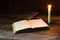 Old antique opened book with burning candle near on the wooden table.