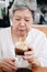 Old asian elderly senior elder woman drinking iced coffee with orange syrup