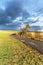 Old asphalt country road between fields. Winter time without snow. Agricultural landscape in the Czech Republic. Dramatic sky