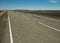 An old asphalt road with white markings and numerous patches stretching