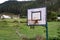 Old basketball hoop in a village court with mountains and forest at the backboard