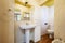 Old bathroom with a lacquered wooden column cabinet, a rectangular frameless mirror, dark stoneware floors and cream-colored tiled