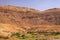 Old berber village oasis with houses build of clay bricks in front of impressive high rugged red mountain face, Gorges du Dades,