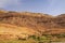 Old berber village oasis with houses build of clay bricks in front of impressive high rugged red mountain face, Gorges du Dades,