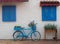 Old blue bicycle stands on the street near the wall with windows with wooden shutters