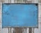 Old blue blank weathered wood noticeboard on rough dirty wall