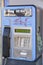 An old blue telephone booth damaged and out of service with signs of deterioration and some banditry painted on it